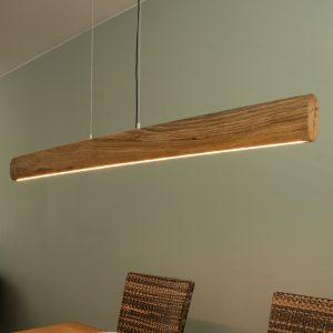 Massief houten hanglamp in natuurlijke Ovale vormige met zichtbare houtnerf en afgeronde uiteinden, voorzien van een subtiel geïntegreerde LED-lichtstrip aan de onderzijde die warm wit licht verspreidt. De lamp hangt aan twee dunne staalkabels en is ideaal als sfeervolle verlichting boven een eettafel of in een modern, landelijk interieur